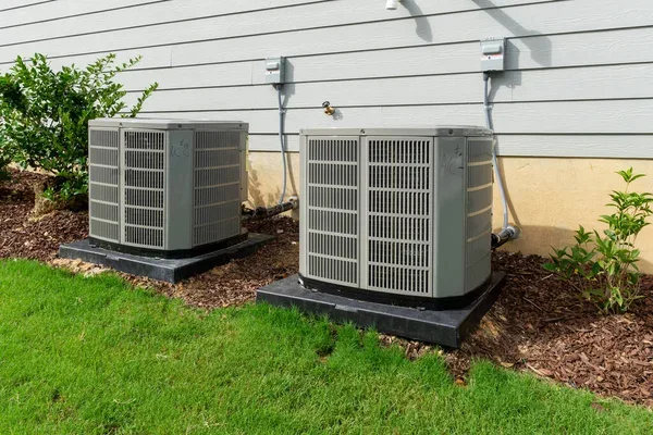 Two residential outdoor air conditioning units beside a house